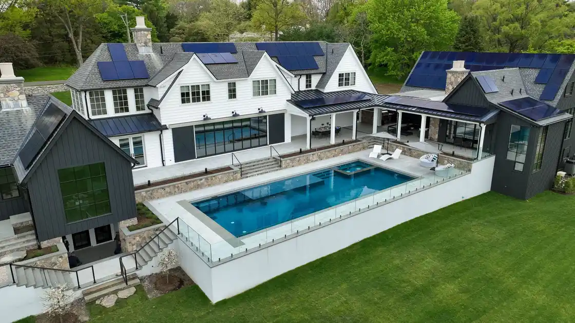 Pool built above grade behind a glass rail beside a modern house