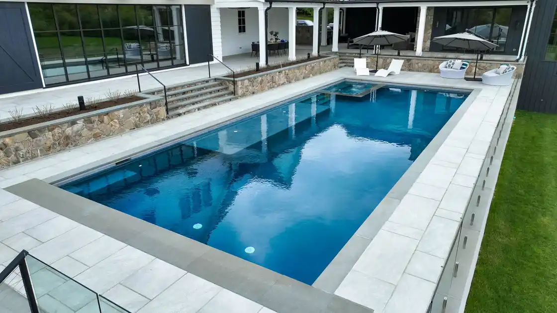 Pool seen from the deck with the house reflected in the water and a stone wall beyond