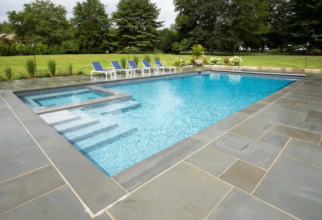 Rectangular pool edged in bluestone with a raised spa and lounge chairs in daylight
