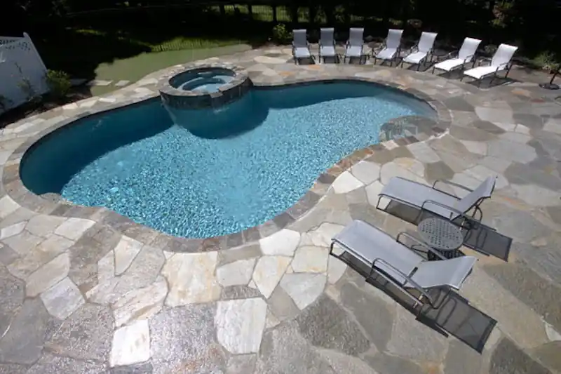 Freeform pool with a raised spa spilling over into it, edged in flagstone