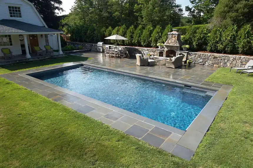 Rectangular pool with bluestone coping beside a stone wall and an outdoor fireplace