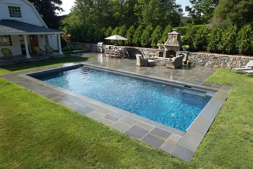 Pool edged in bluestone with an outdoor fireplace and kitchen behind