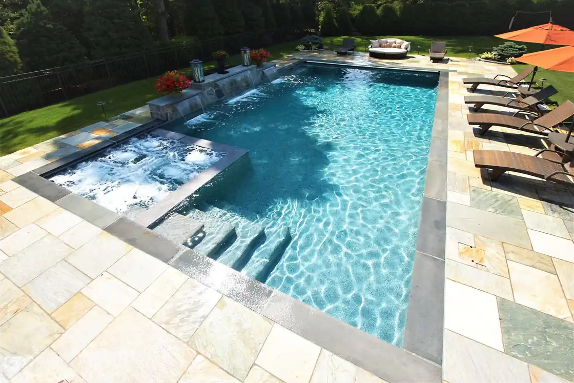 Long pool with a waterfall wall, a spa and lounge chairs on flagstone