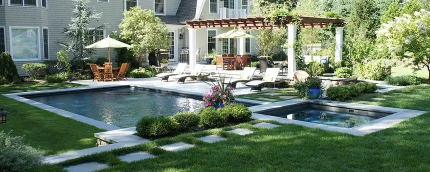 Pool beside a pergola and patio with a lush garden behind